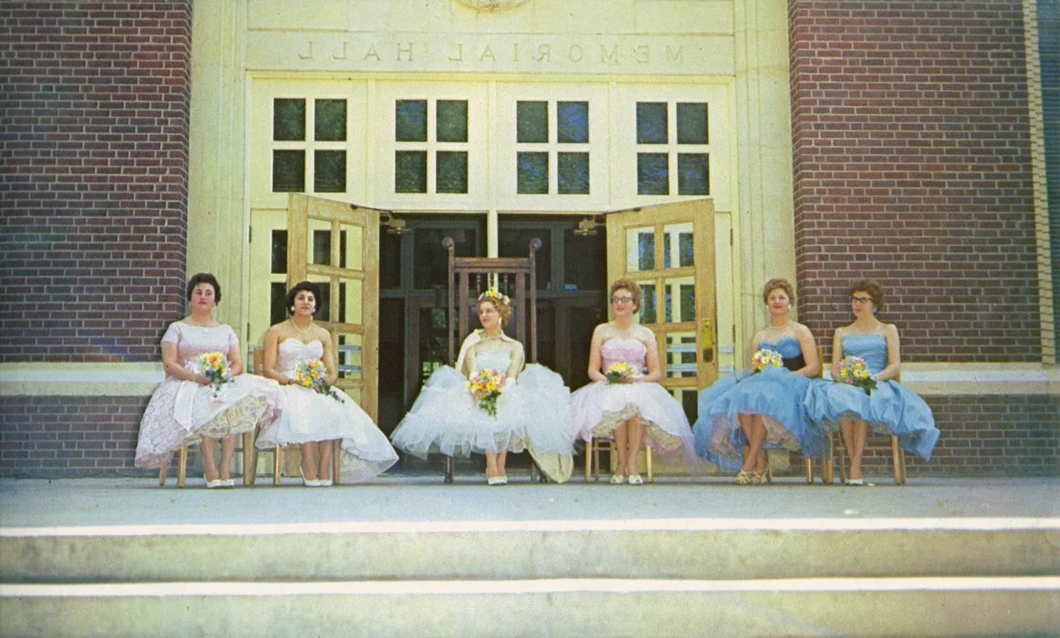 Four students wearing formal gowns in front of an academic building